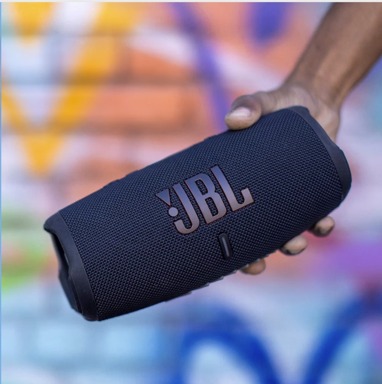 A dark JBL portable speaker held in a hand